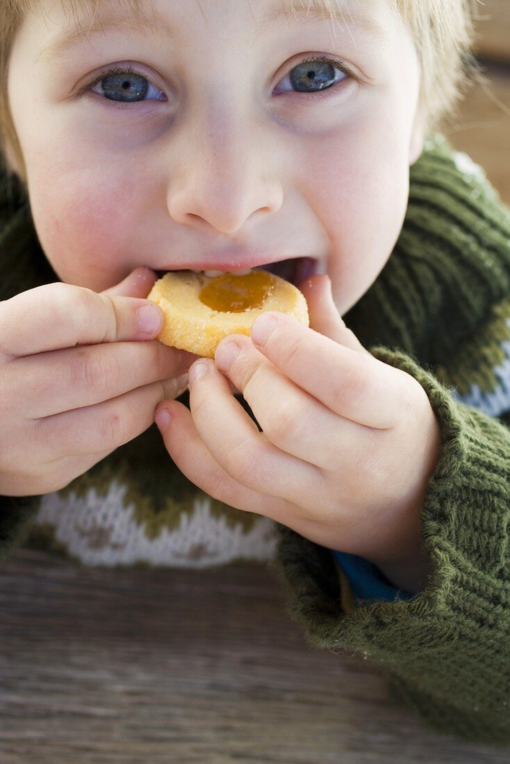 Small boy biting into a jam biscuit