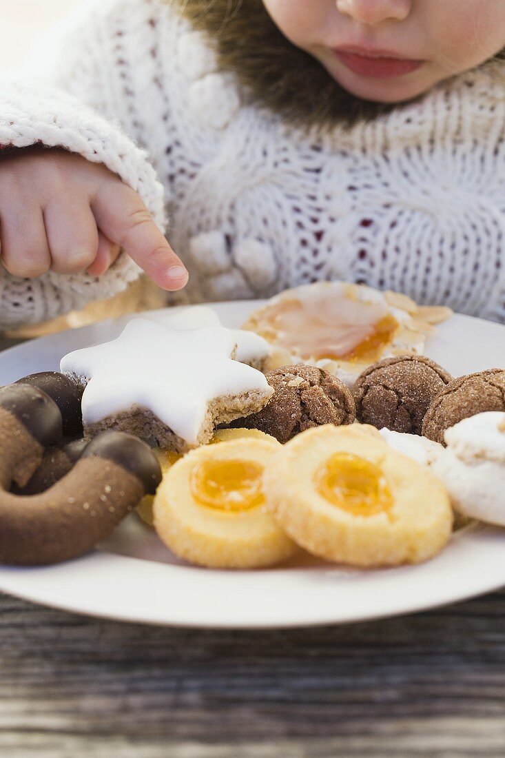 Kleines Mädchen greift nach Weihnachtsplätzchen auf Teller