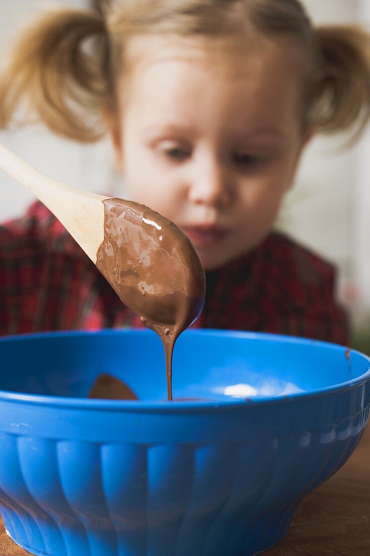 Chocolate icing running from wooden spoon, child in background