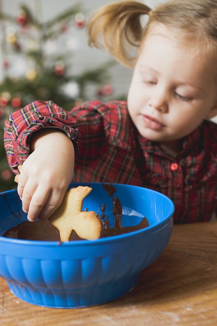 Mädchen taucht Weihnachtsplätzchen in Schokoladenglasur