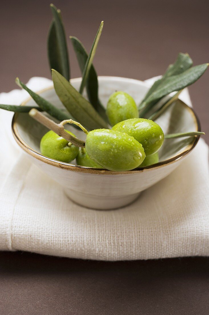 Grüne Oliven am Zweig in Schale auf Leinentuch