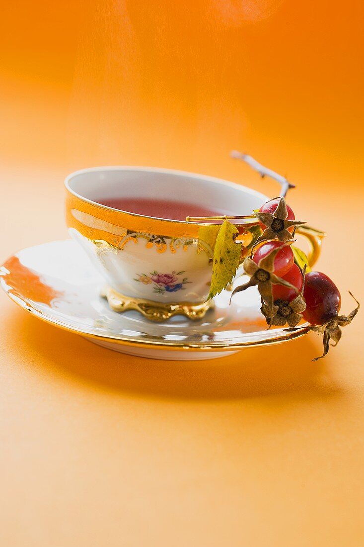 Rose hip tea in china cup, fresh rose hips in saucer