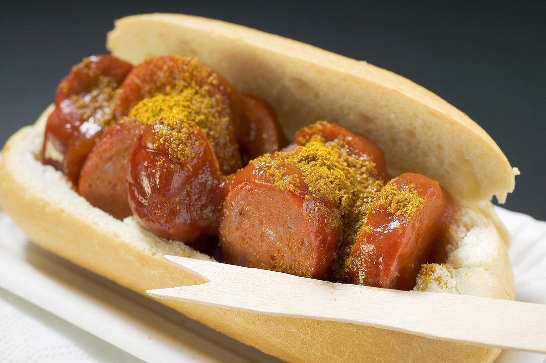 Sausage with ketchup & curry powder in bread roll in paper dish