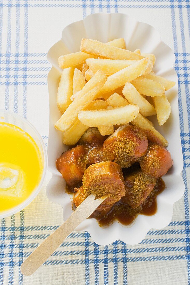 Currywurst mit Ketchup und Pommes frites auf Pappteller, Limo