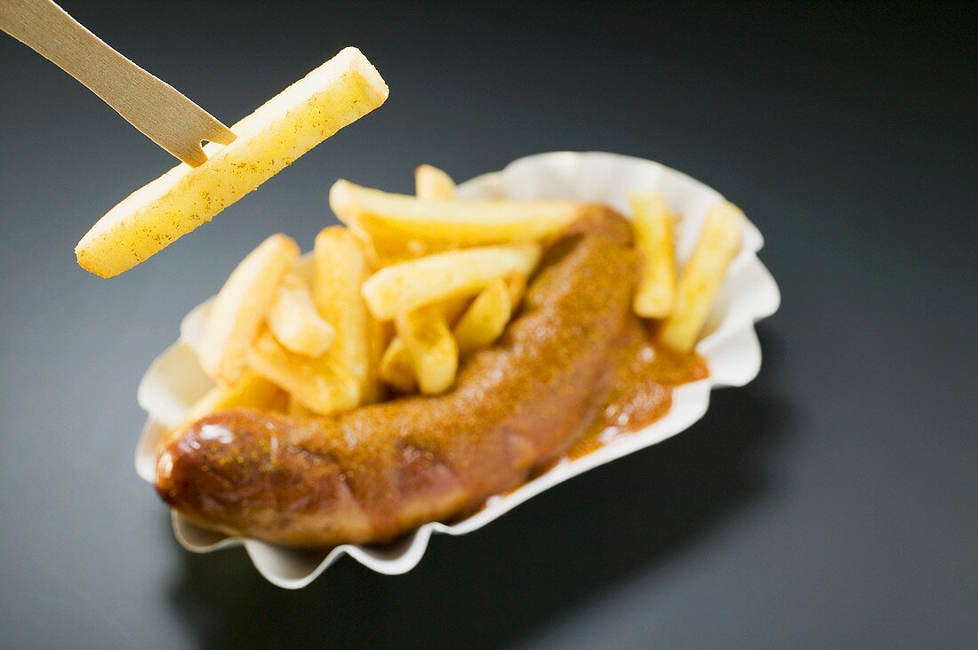 Ssausage with ketchup & curry powder & chips, one on wooden fork