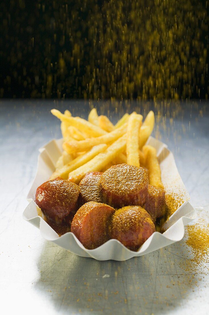 Currywurst mit Pommes frites mit Curry bestreuen