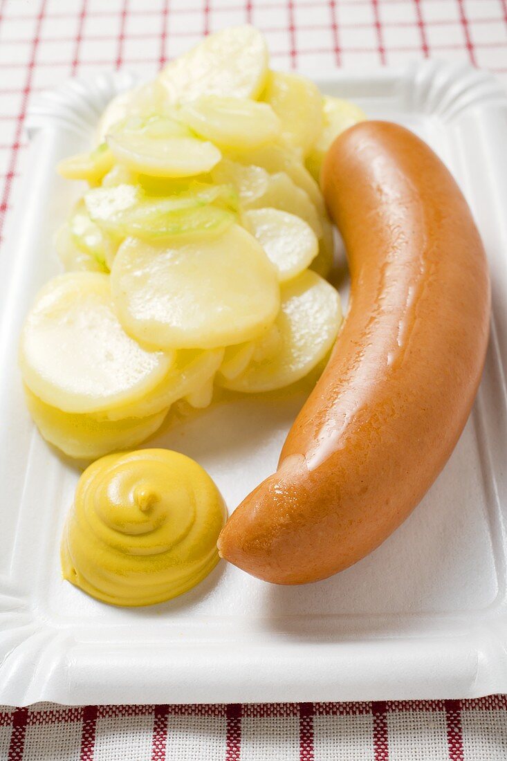Frankfurter with potato salad and mustard on paper plate