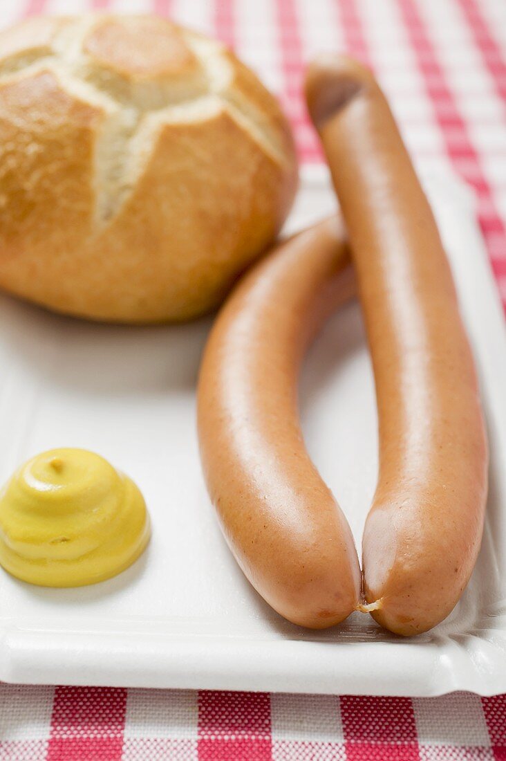 Frankfurters with mustard and bread roll on paper plate