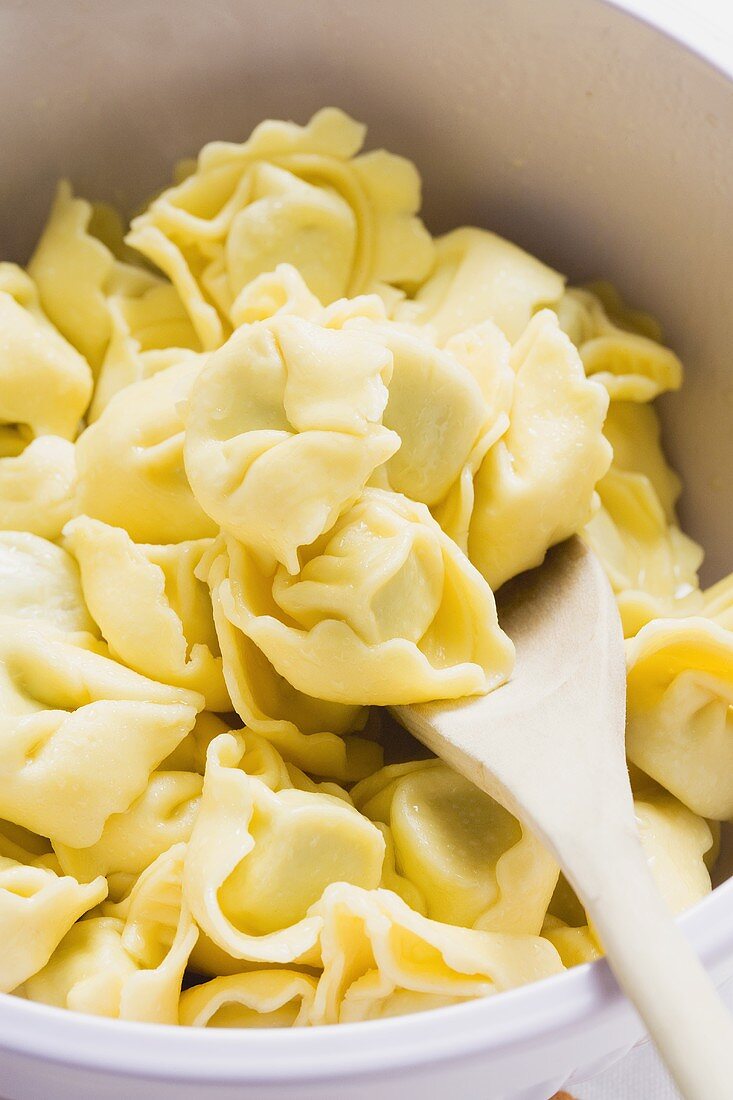 Tortellini in white bowl with wooden spoon (detail)