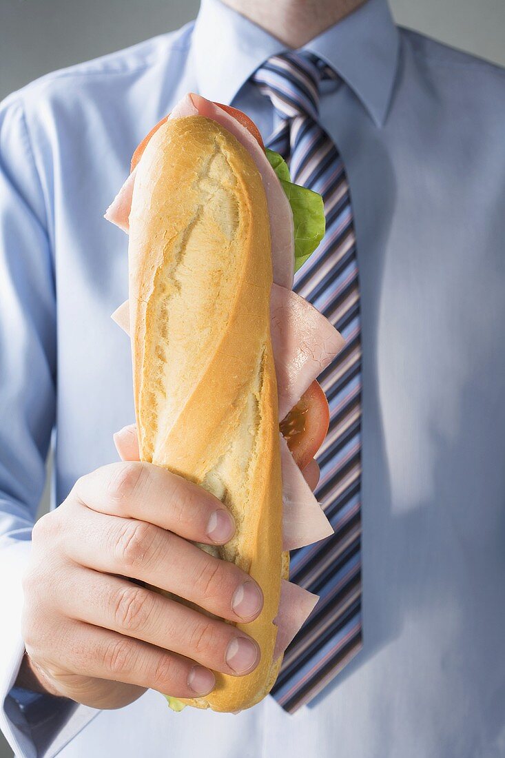 Man in tie holding ham sub sandwich