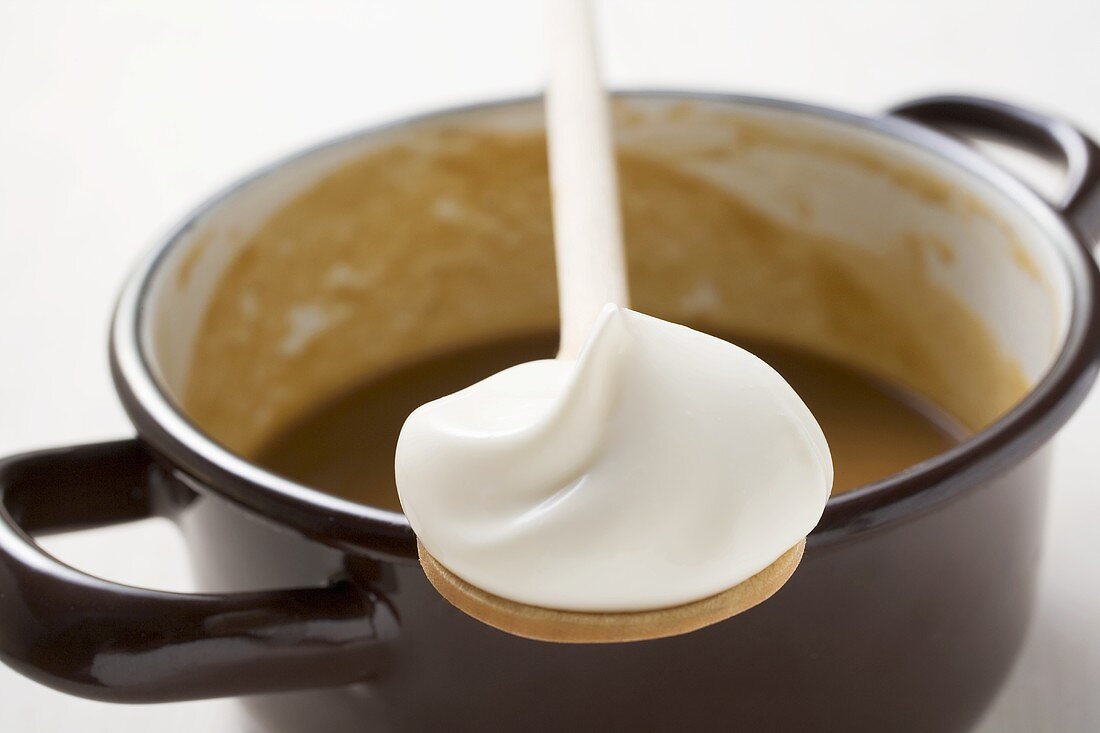 Gravy in pan, wooden spoonful of crème fraîche resting on pan