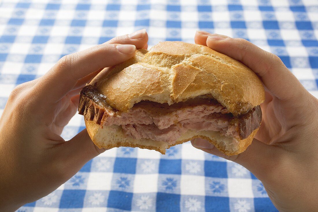 Hands holding Leberkäse in bread roll, partly eaten