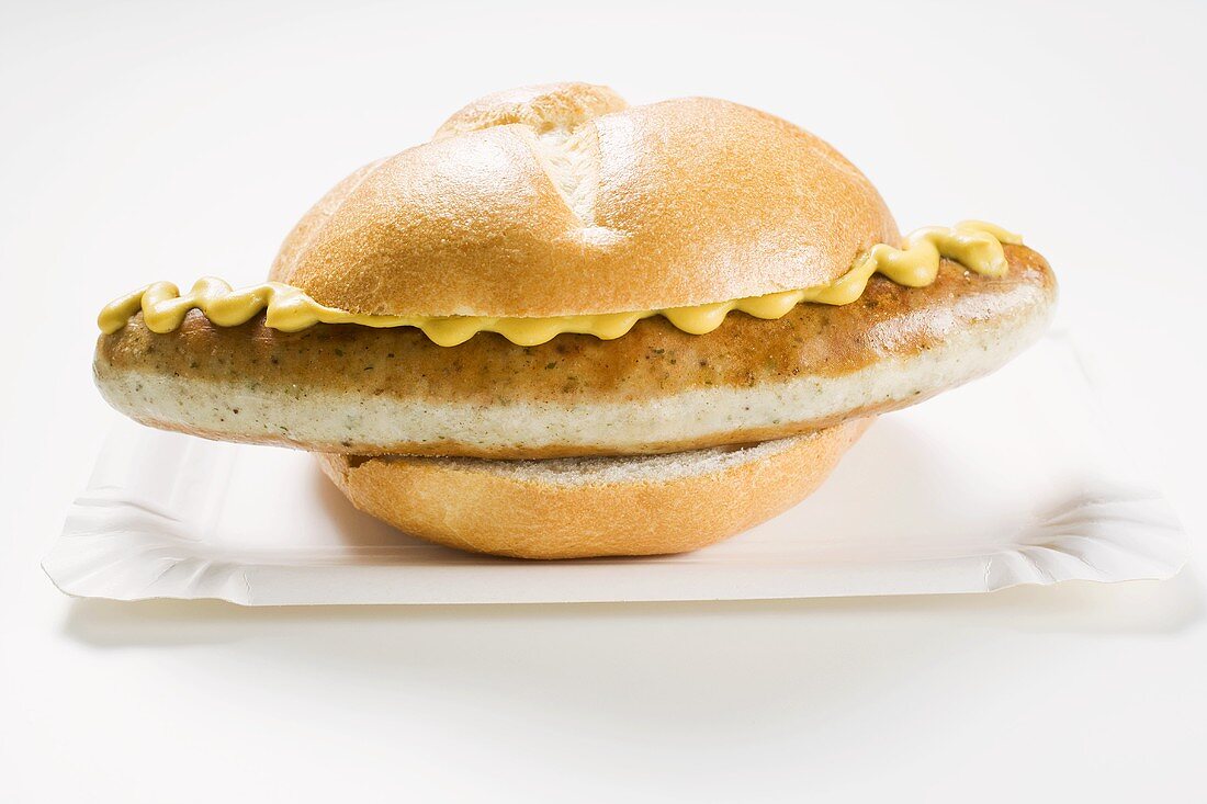 Sausage and mustard in bread roll on paper plate