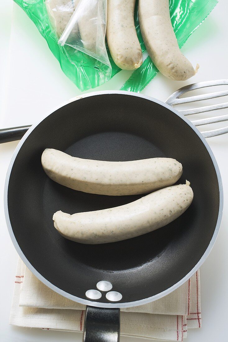 Frische Bratwürste in Pfanne und geöffneter Verpackung