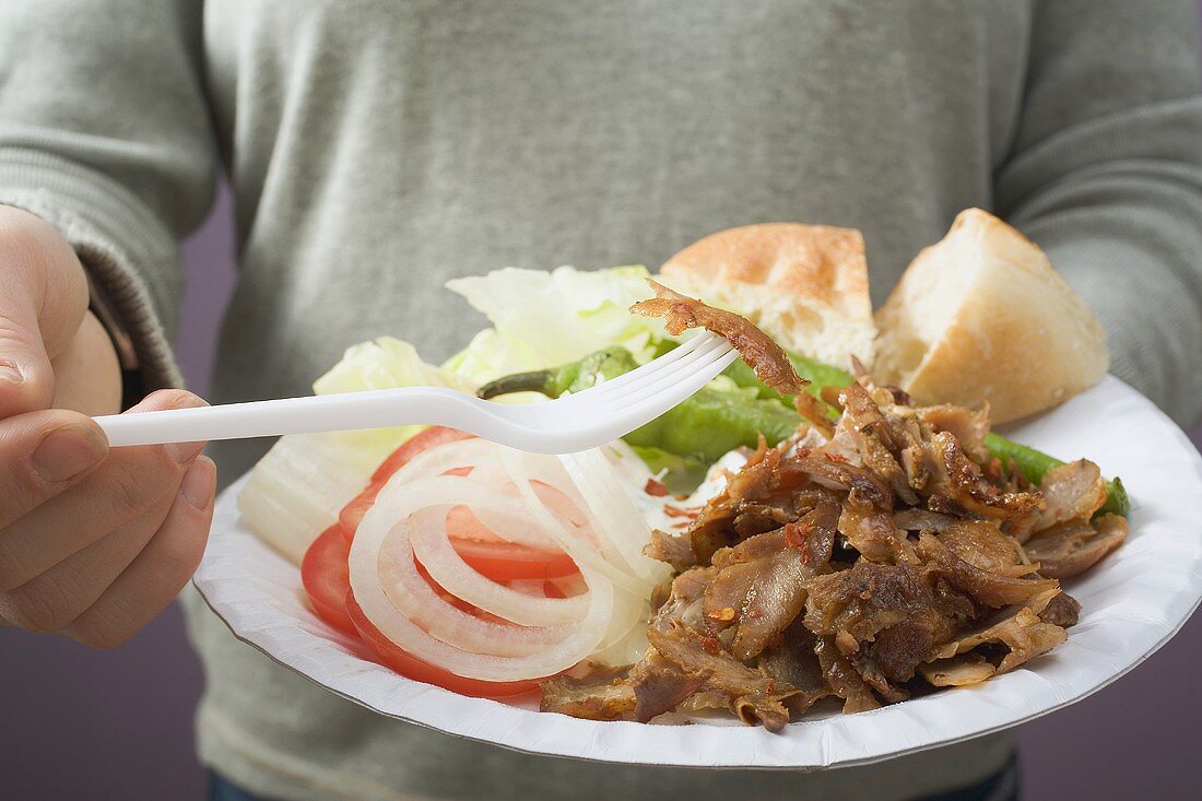 Frau hält Pappteller mit Döner Kebab, Gemüse und Fladenbrot