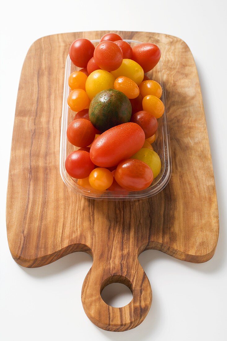 Verschiedene Tomaten in Plastikschale auf Schneidebrett