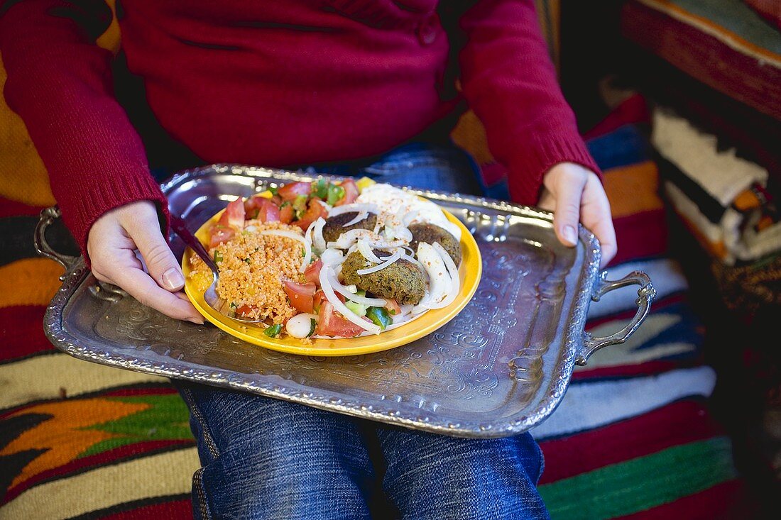 Person holding falafel with accompaniments on tray (N. Africa)