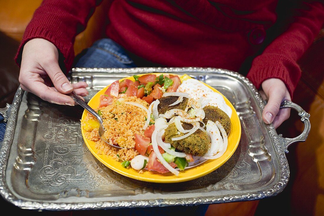 Person holding falafel with accompaniments on tray (N. Africa)