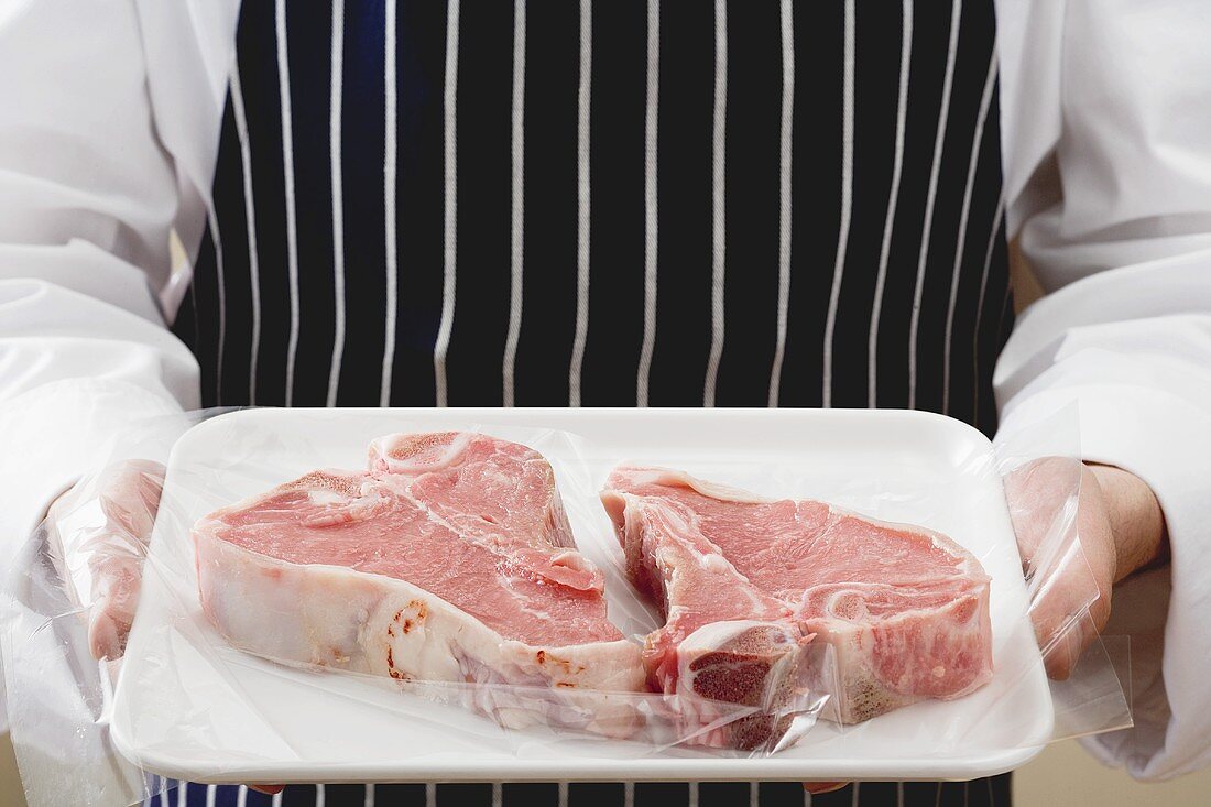 Person holding two T-bone steaks on tray