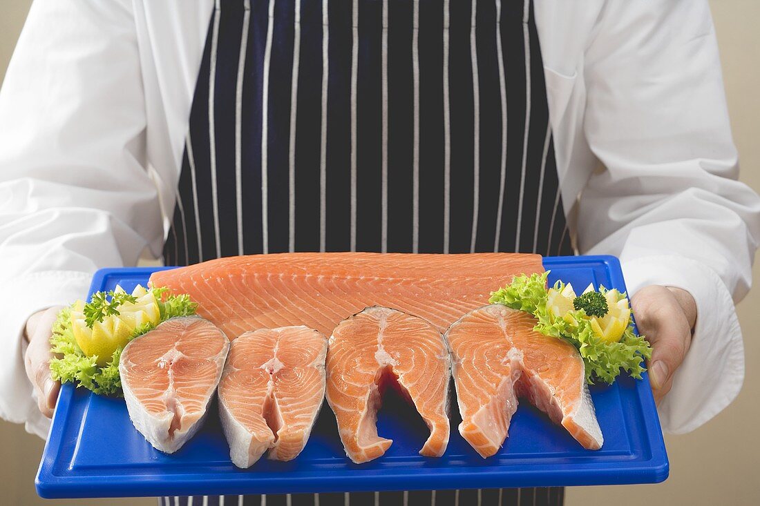 Person holding various cuts of salmon on chopping board