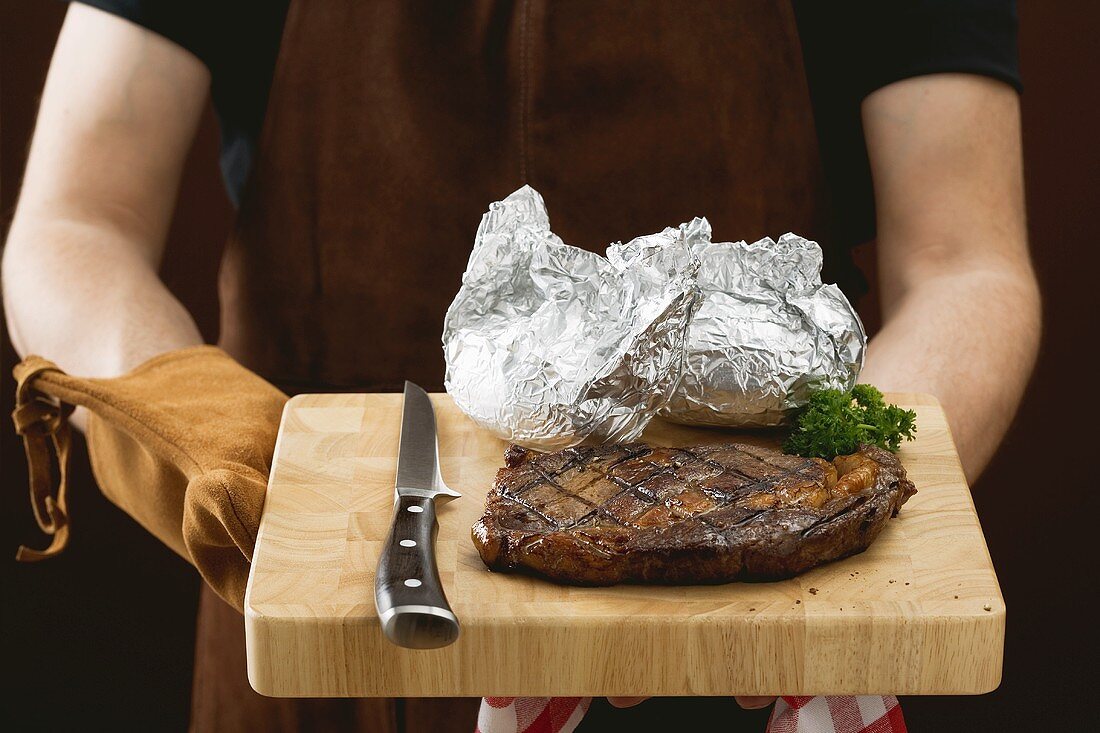 Mann hält Schneidebrett mit gegrilltem Rindersteak