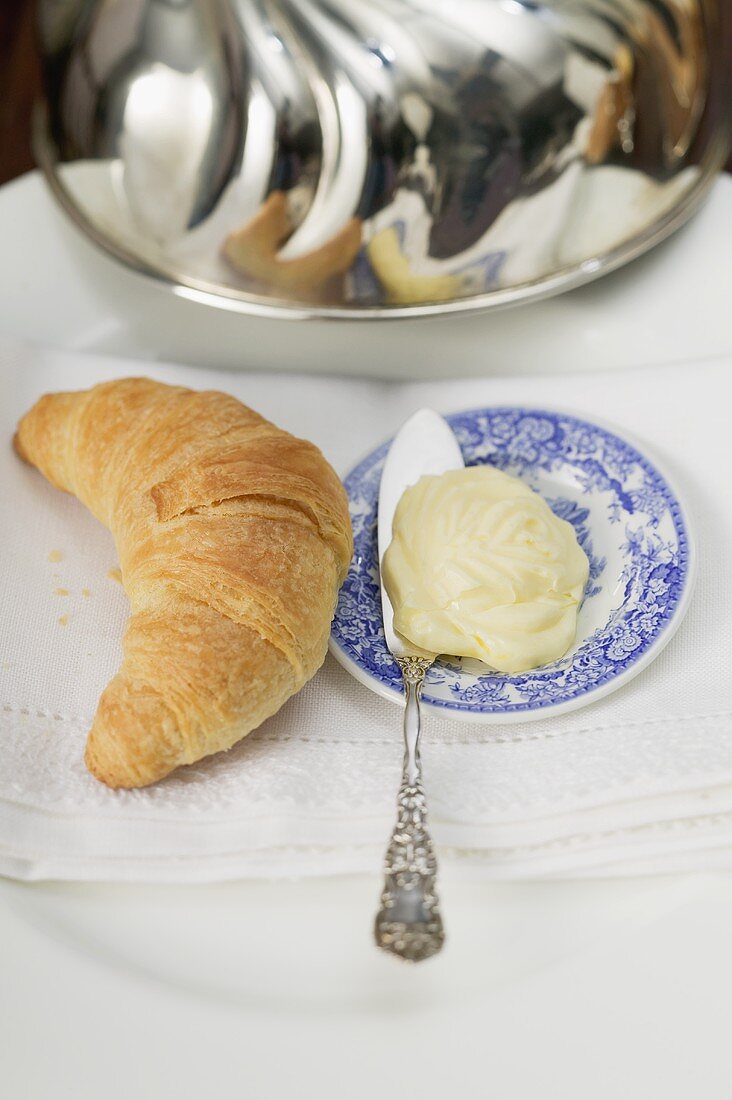 Croissant neben Teller mit Butter und Messer