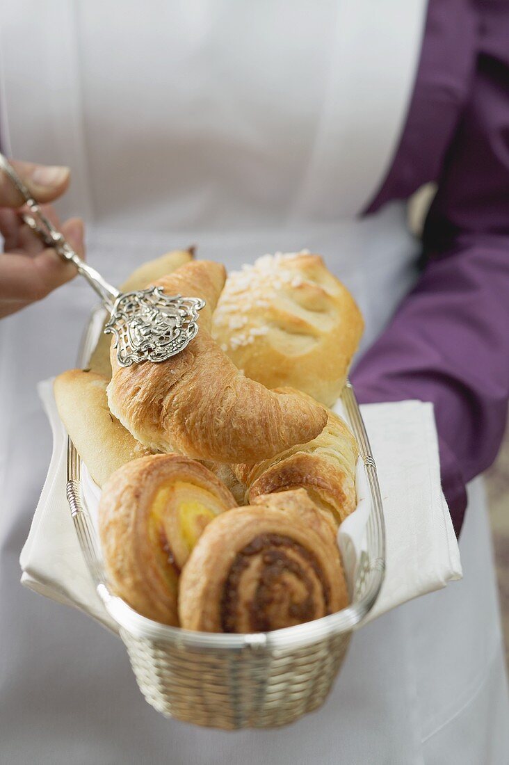 Chambermaid serving breakfast pastries from bread basket