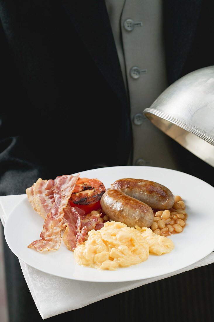 Butler serviert englisches Frühstück auf Teller mit Cloche