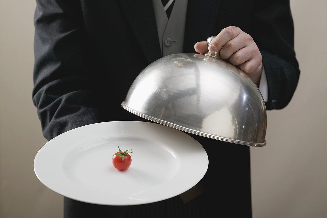 Butler serving cherry tomato on plate with dome cover