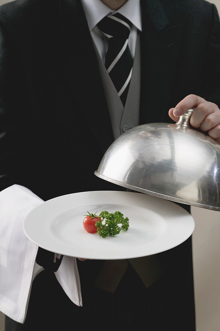Butler serviert Tomate und Petersilie auf Teller mit Cloche
