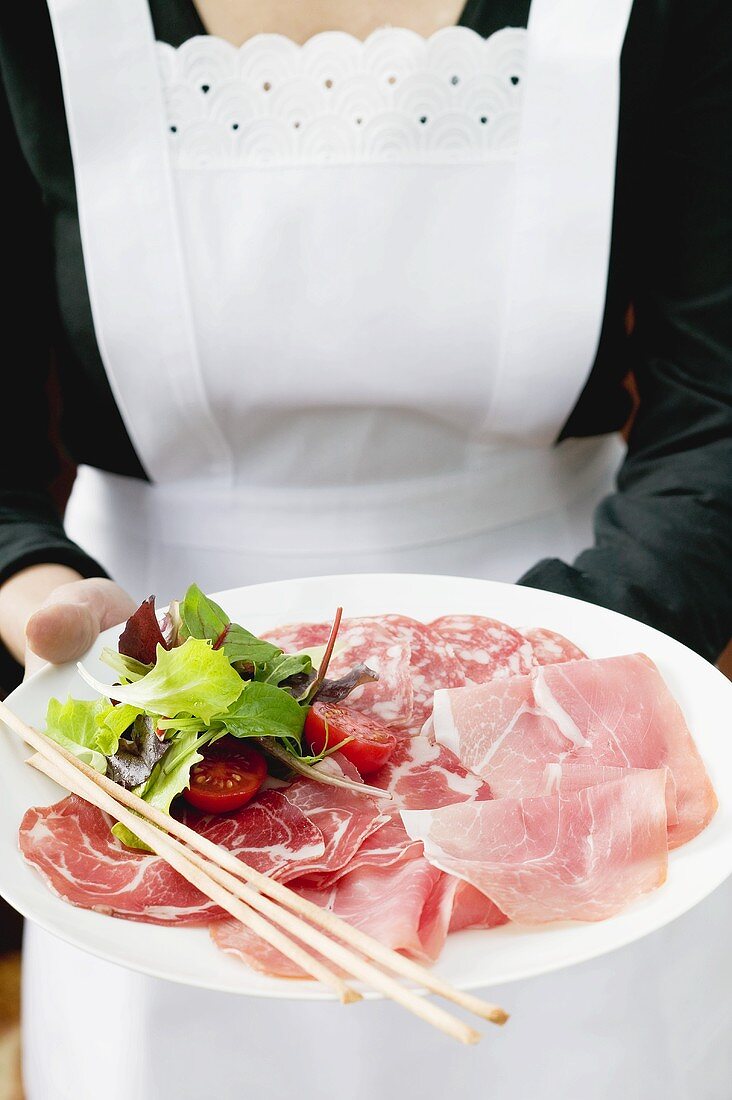 Waitress serving Italian sausage platter with grissini