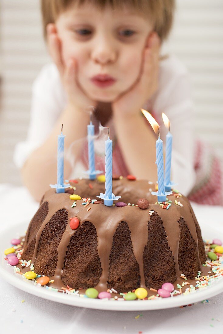 Kleiner Junge bläst Kerzen am Geburtstagskuchen aus