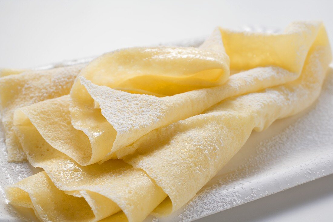 Wafer-thin crêpes with icing sugar on paper plate