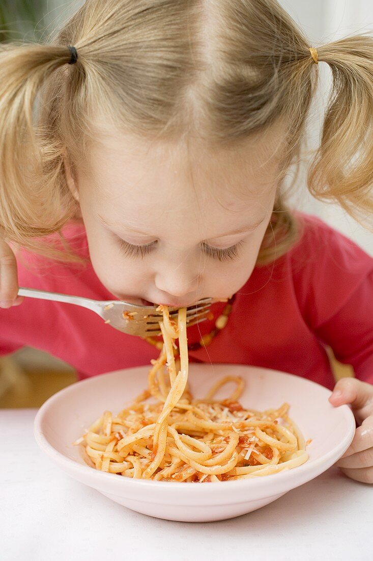 Small girl eating noodles with tomatoes