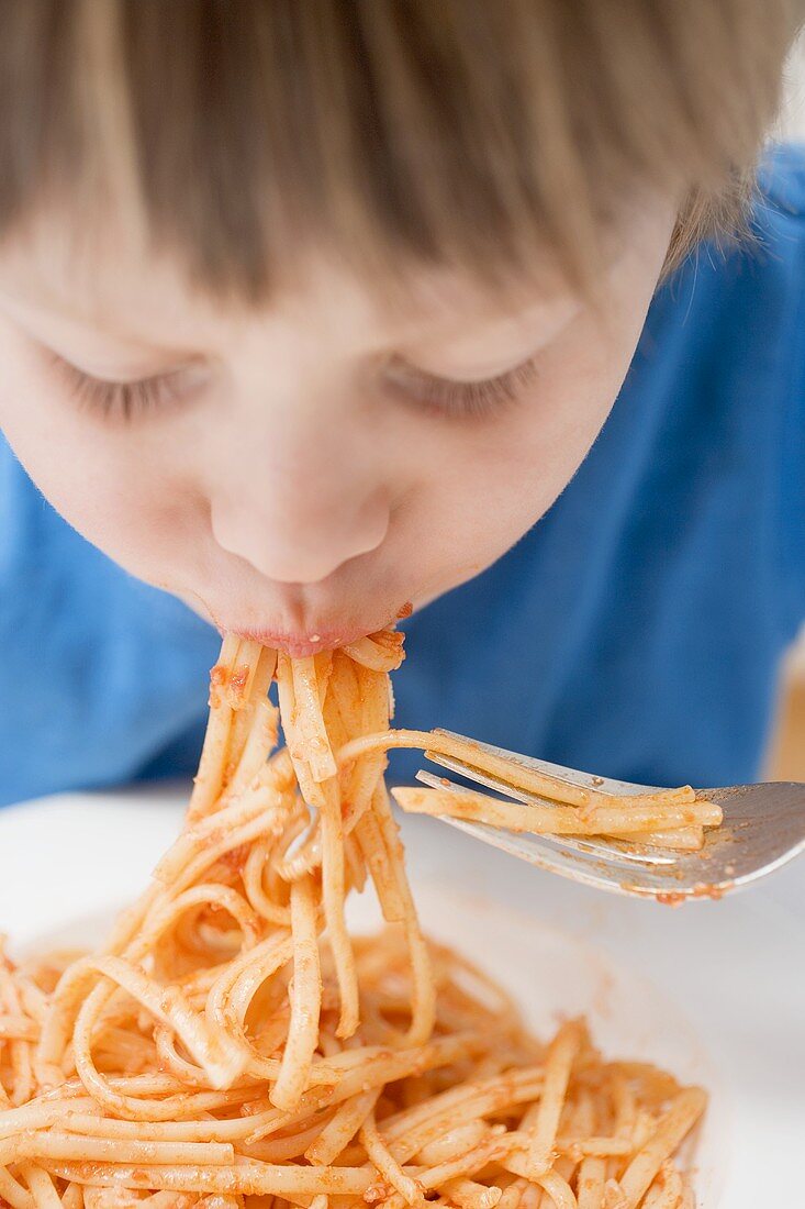 Small boy eating noodles with tomatoes