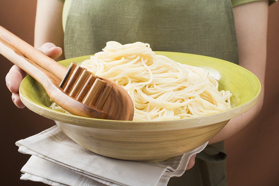 Woman holding bowl of cooked spaghetti