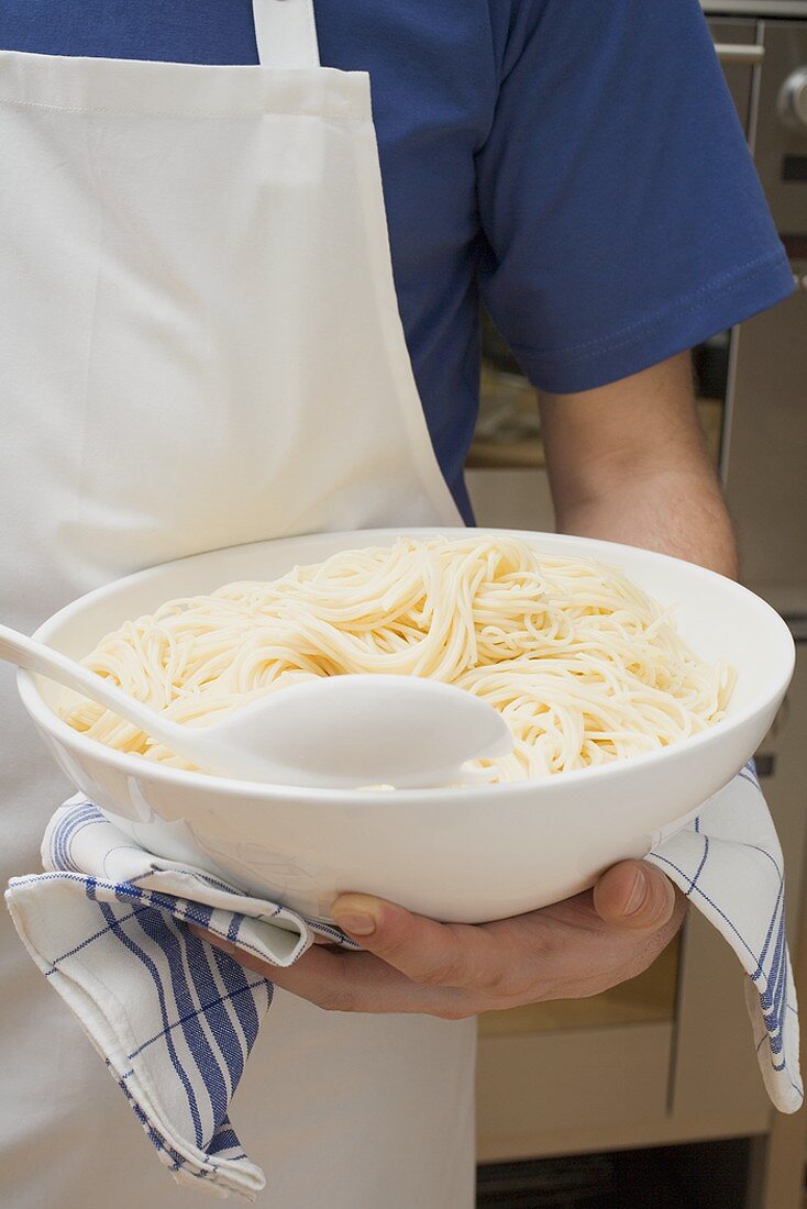 Person holding bowl of cooked spaghetti
