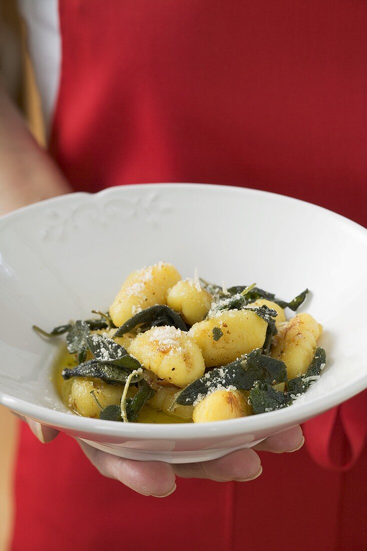 Hand hält Teller mit Gnocchi in Salbeibutter