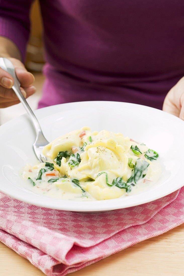 Frau isst Tortellini mit Spinat und Sahnesauce