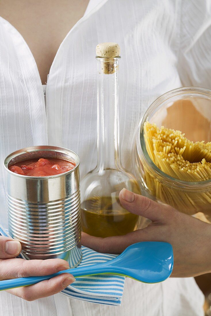 Woman holding spaghetti, tin of tomatoes, olive oil & spoon