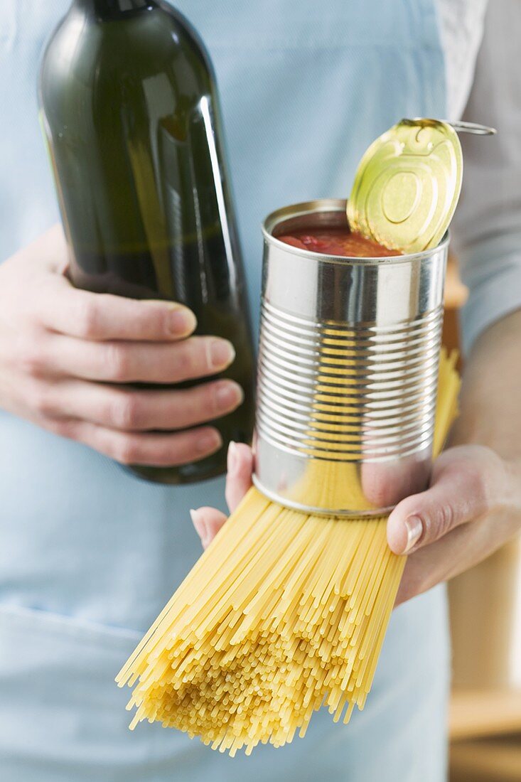 Frau hält Spaghetti, Dosentomaten und Weinflasche