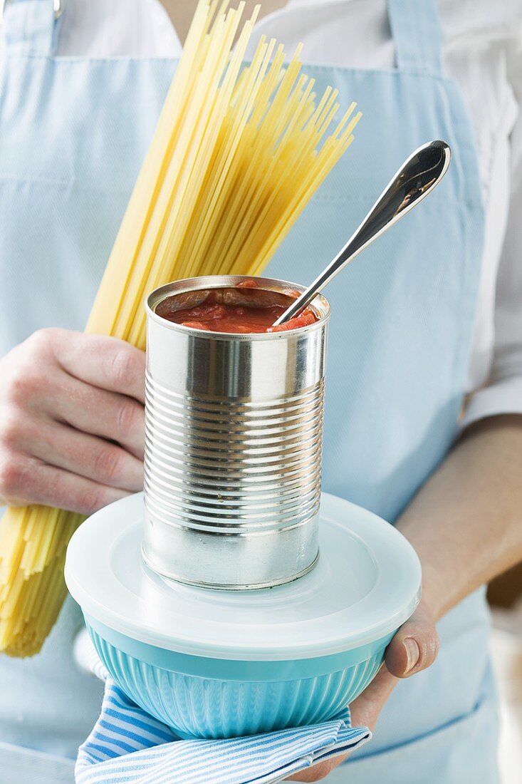 Frau hält Spaghetti, Dosentomaten und Frischhaltedose