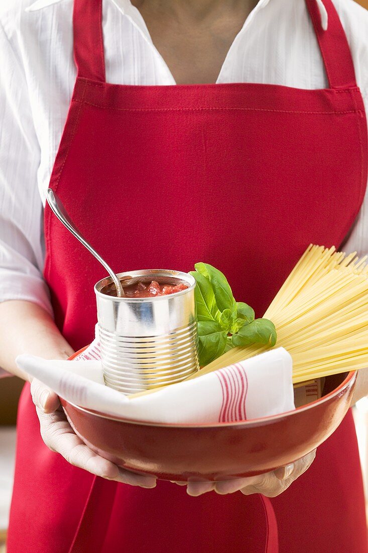 Frau hält Dosentomaten, Spaghetti und Basilikum