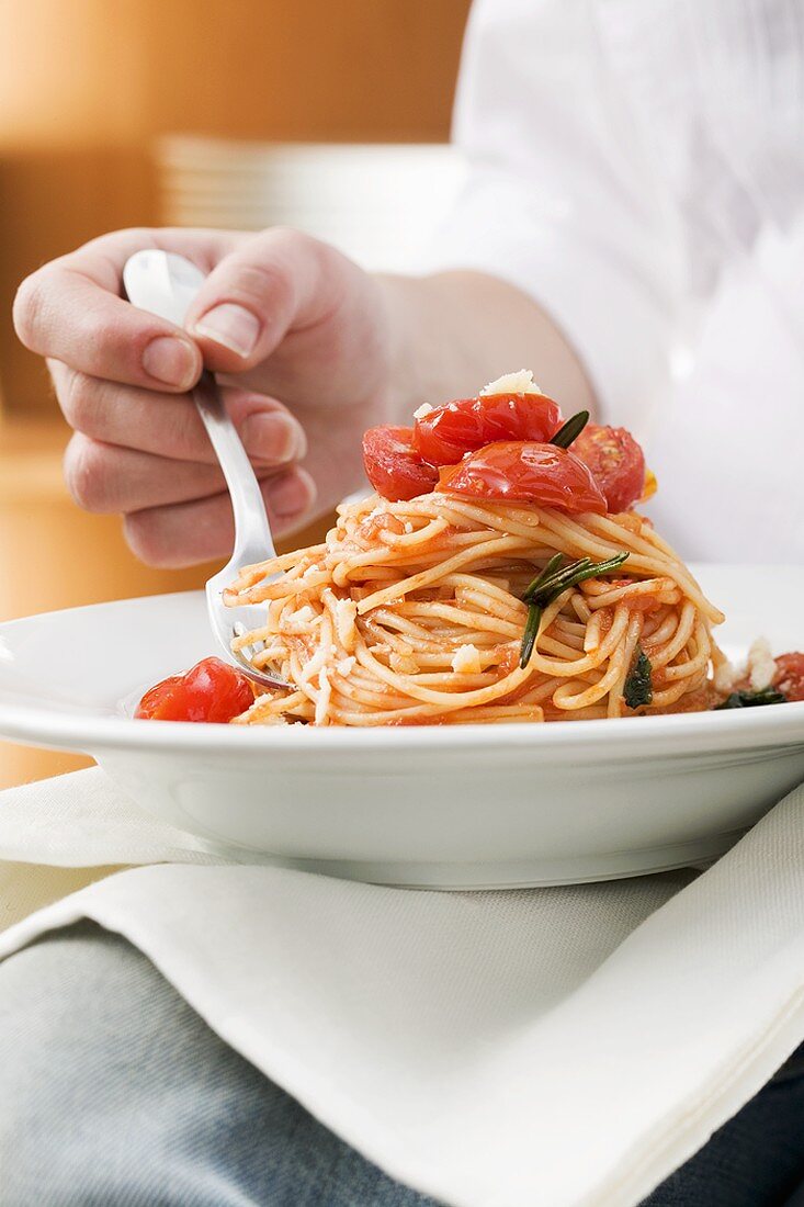 Person isst Spaghetti mit Tomaten und Rosmarin