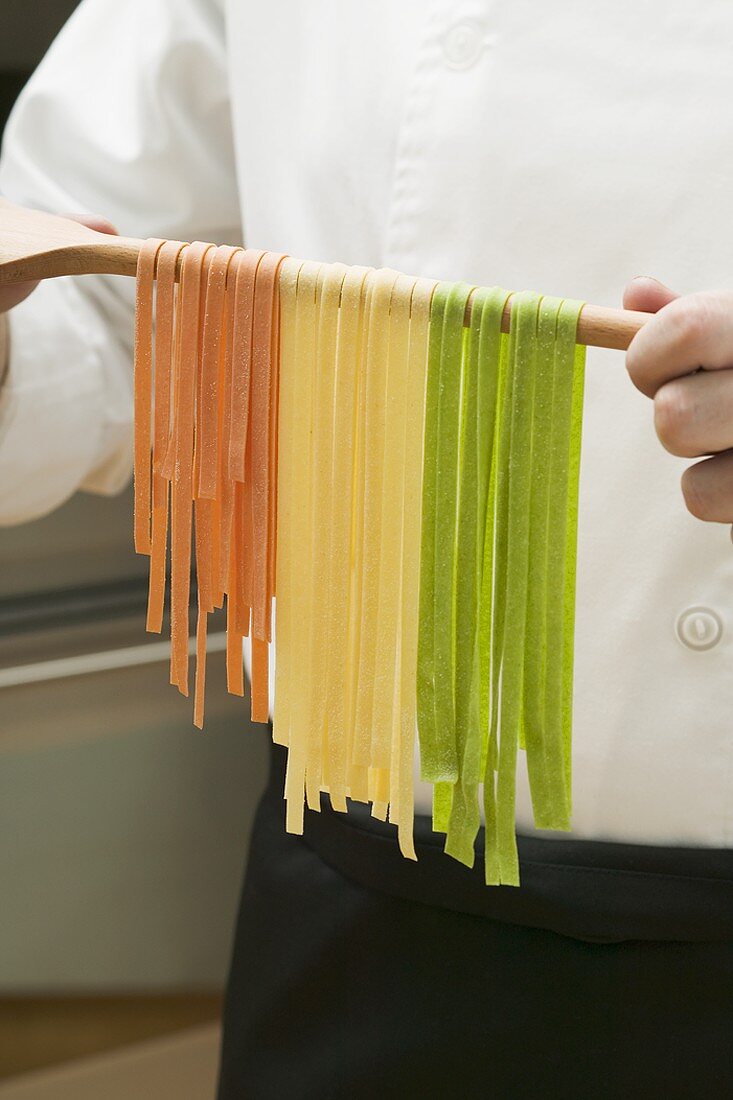 Home-made ribbon pasta hanging over wooden spoon