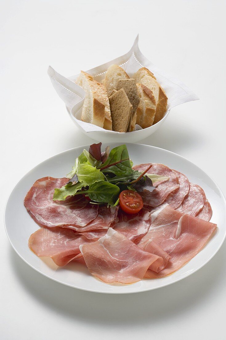 Raw ham and salami on plate, baguette slices