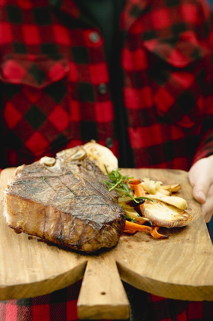 Mann serviert gegrilltes T-Bone-Steak auf Schneidebrett