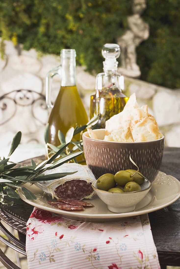 Oliven, Salami, Cracker und Olivenöl auf Tisch im Freien