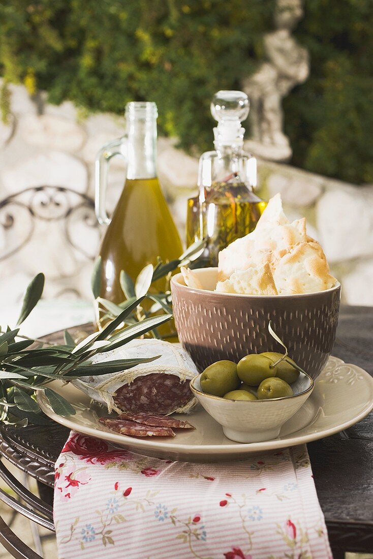Olives, salami, crackers & olive oil on table out of doors