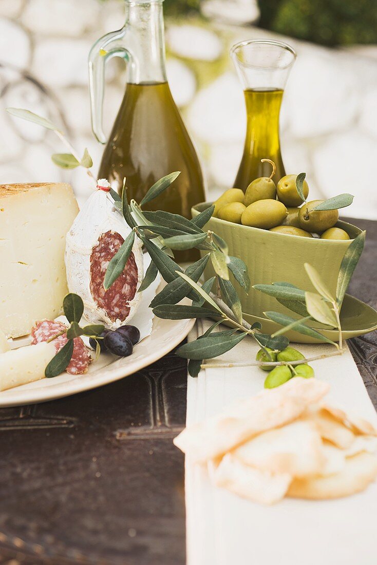 Käse, Salami, Oliven, Olivenöl, Cracker auf Tisch im Freien